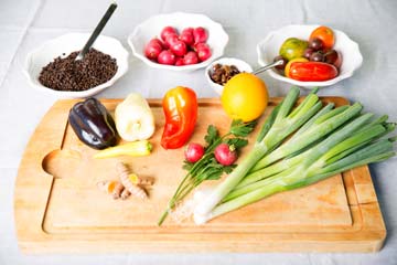 Jungzwiebel, verschiedene Paprika, Tomaten, Linsen, Radieschen, Oliven, Kurkuma und Kräuter auf einem Schneidbrett und in kleinen Schalen